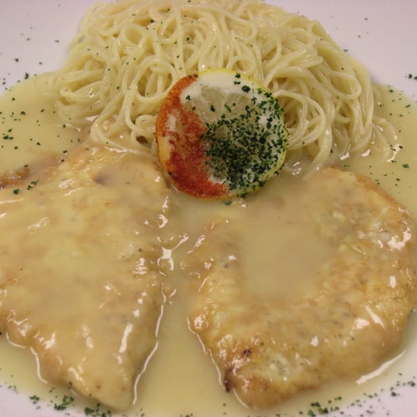 Chicken Francese with spaghetti and lemon slice, garnished with parsley and paprika.