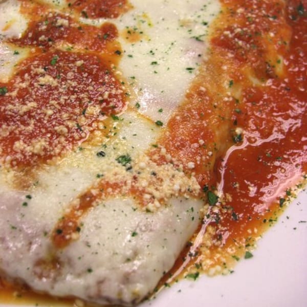 Close-up of baked Italian dish with melted cheese, red sauce, and sprinkled herbs.