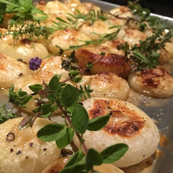 Close-up of roasted onions garnished with fresh herbs, including rosemary, thyme, and oregano.